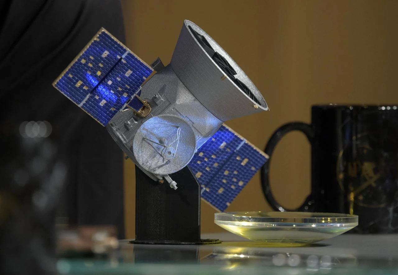 A TESS model and spare camera lens at a NASA briefing. Ground photograph of mission hardware.